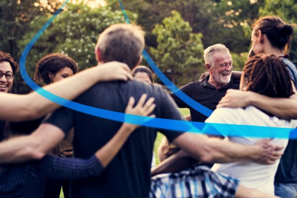 Photo of people of all ages embracing in a circle, with a blue ribbon connecting them