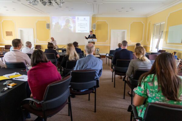 Delegates at the conference facing away from the camera towards a speaker who is standing on a stage.