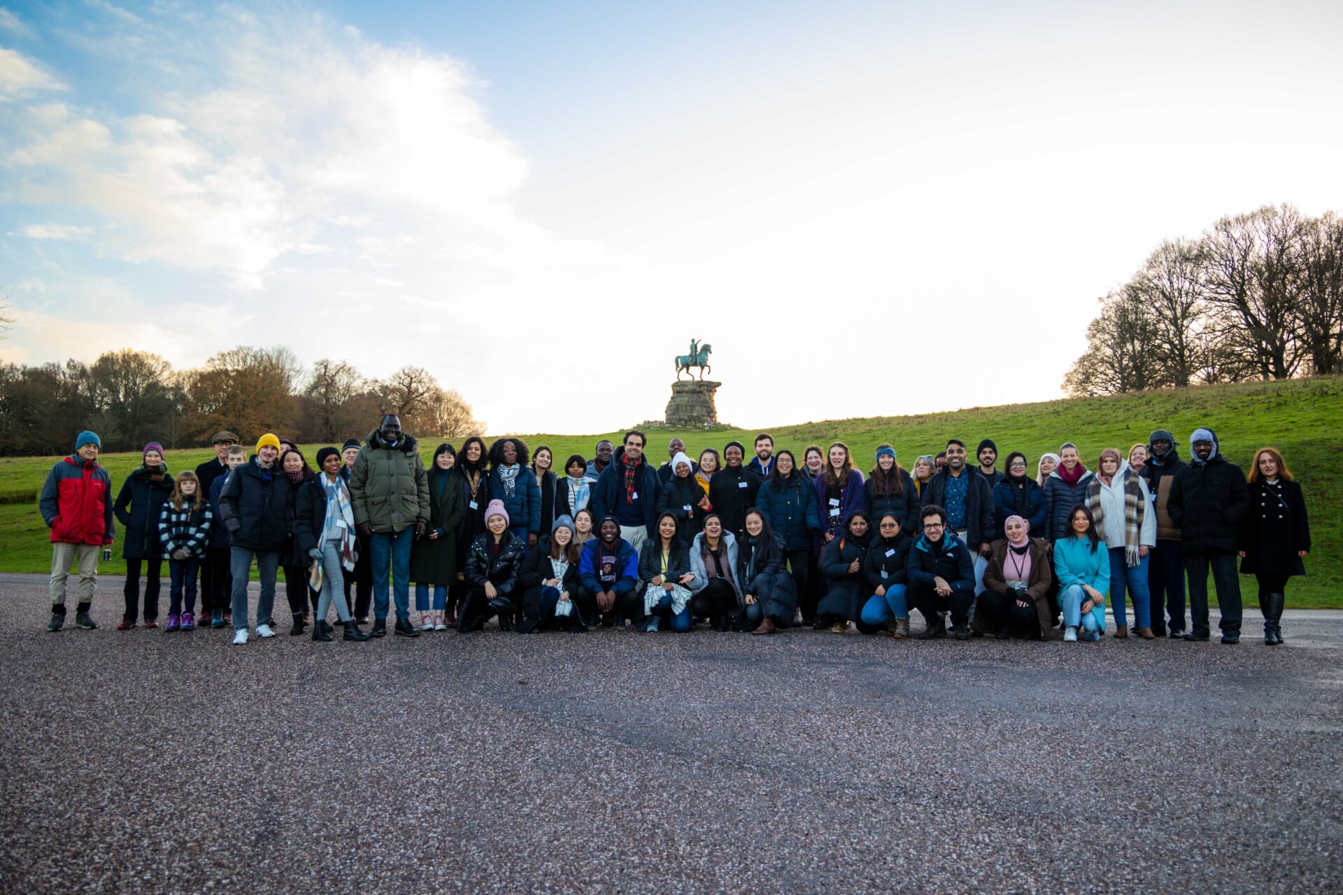 Participants at our Christmas conference posing for a photo in Windsor Great Park, with the Copper Horse statue behind them, as the sun is setting.