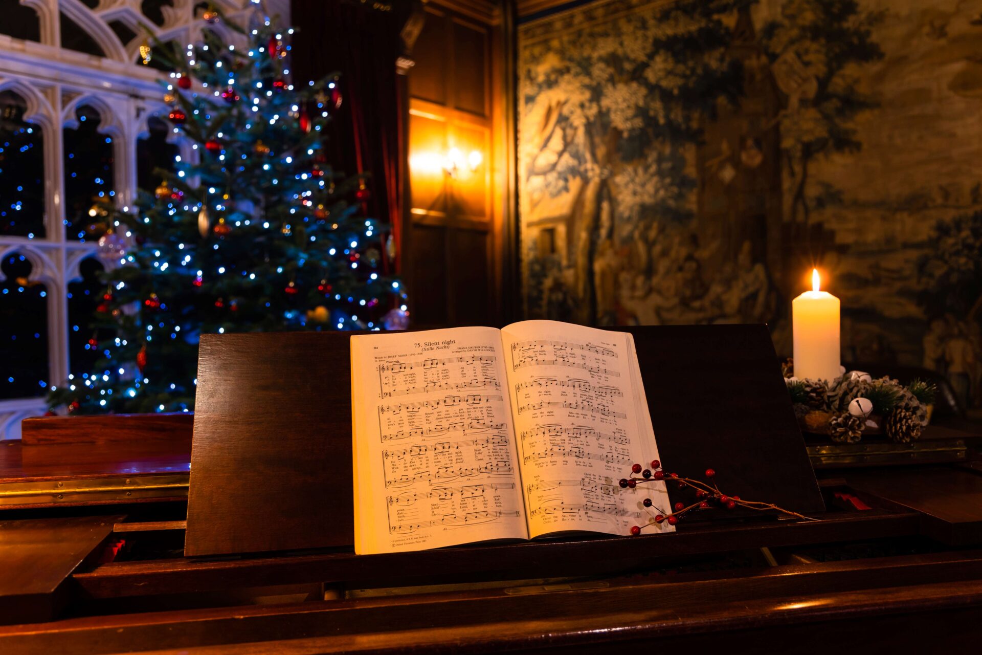 Festive sheet music on a piano, in front of a Christmas tree, in the Tapestry Hall in Cumberland Lodge