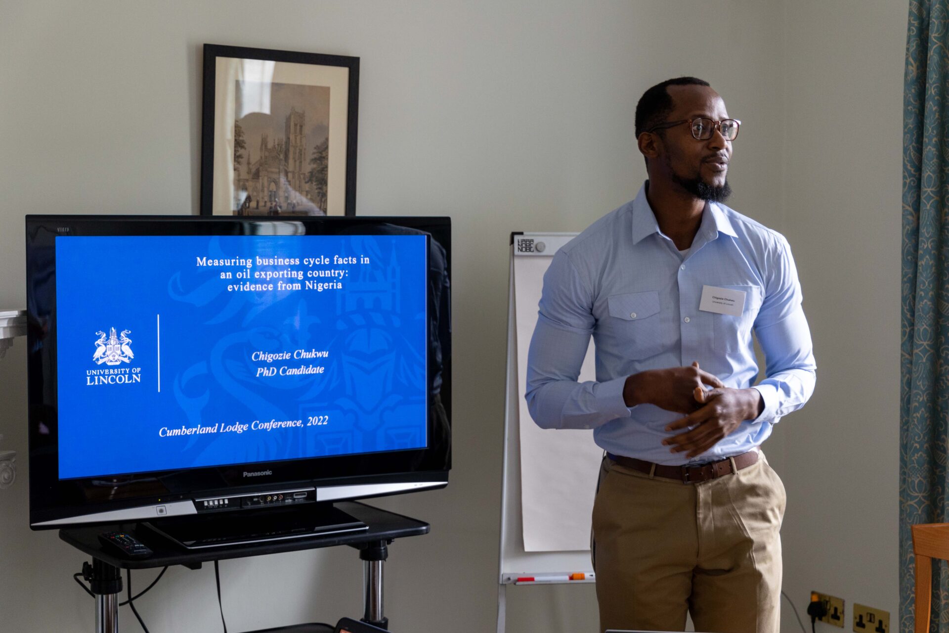 A student stands next to a television screen containing slides from a presentation they are delivering.