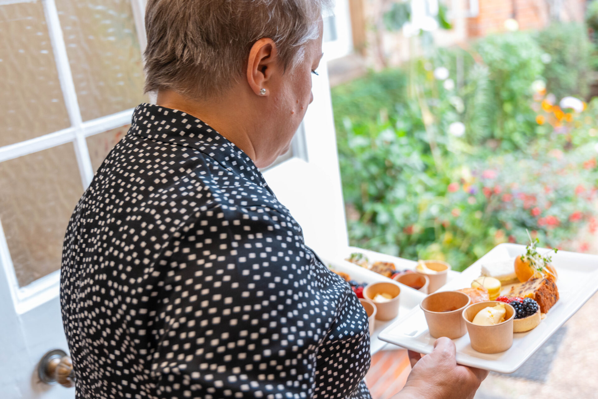 A member of the dining team carries afternoon tea plates into the garden
