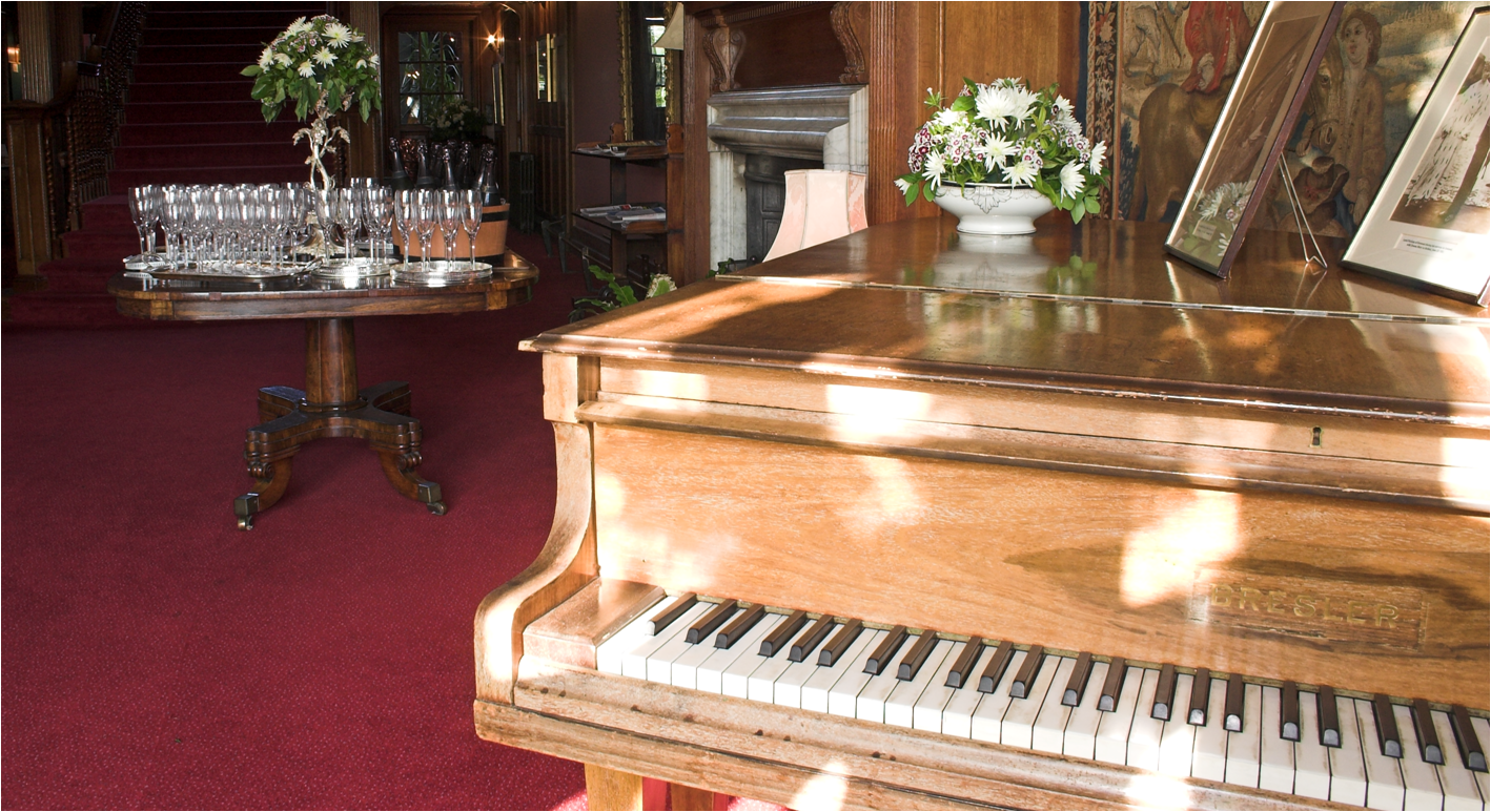 A close up on the piano in the Tapestry Hall, with glasses for a drinks reception set up in the background.