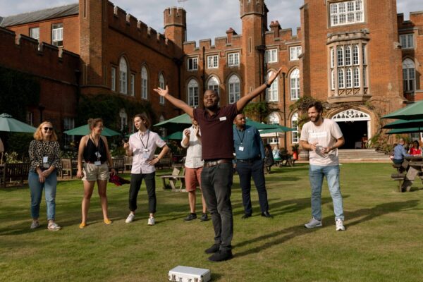 A group of Fellows playing croquet on the lawn outside the Lodge. One has his arms in the air, celebrating.
