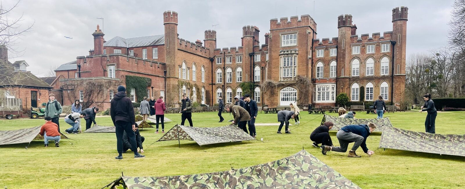 A group taking part in a team-building activity involving tents on the lawn with Cumberland Lodge in the background.