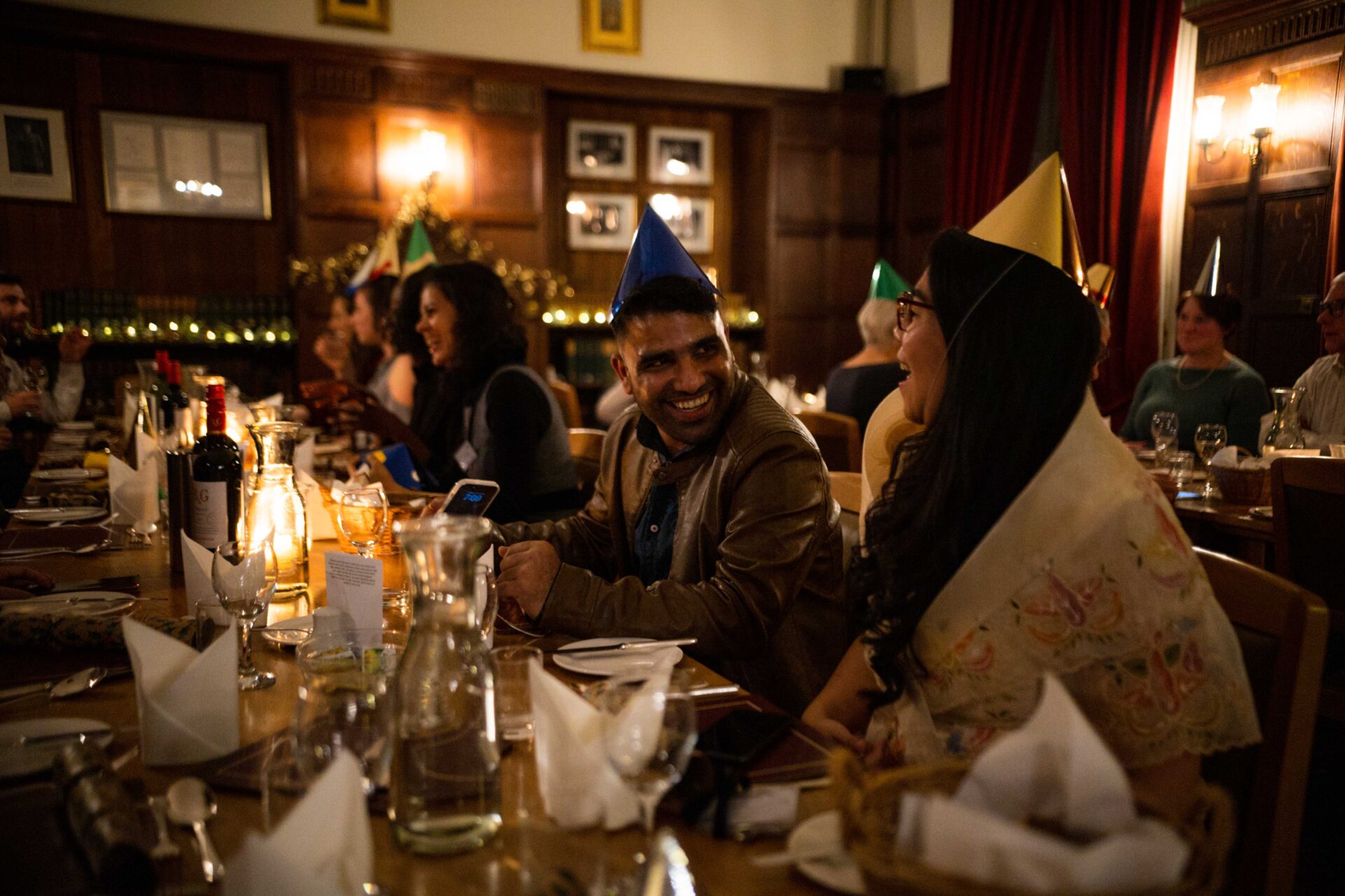 Students wearing party hats having Christmas dinner in a candlelit dining room.